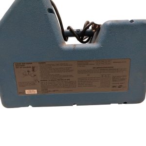 Blue portable device with a coiled power cord visible and a large warning/specification label on the side, viewed from the back.