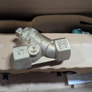 Silver three-way metal pipe fitting (tee) with hex ends, resting on cardboard. Has stamped numbers/letters on the surfaces.