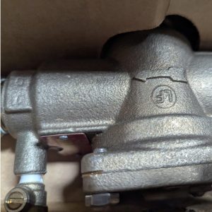 Close-up of a metallic plumbing pressure regulator with a visible crack along the joint and a small screw at the lower left.