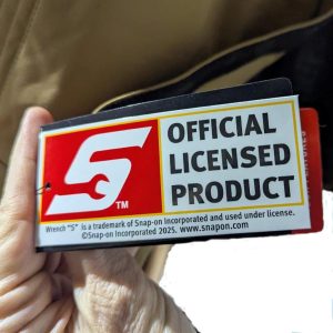 Close-up of a hand holding a Snap-on 'Official Licensed Product' badge with a red logo on the left and bold text on the right.