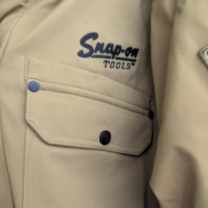 Beige work jacket with Snap-on Tools logo on the chest area and a front pocket with blue button