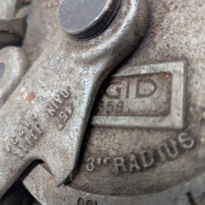 Ridgid-358-Model-Geared-Ratchet-Tube-Bender_10 | Chicago HVAC tools and supplies Close-up of a weathered metal latch with stamped numbers and a small rectangular label reading 'ID' on a dusty mechanical part.