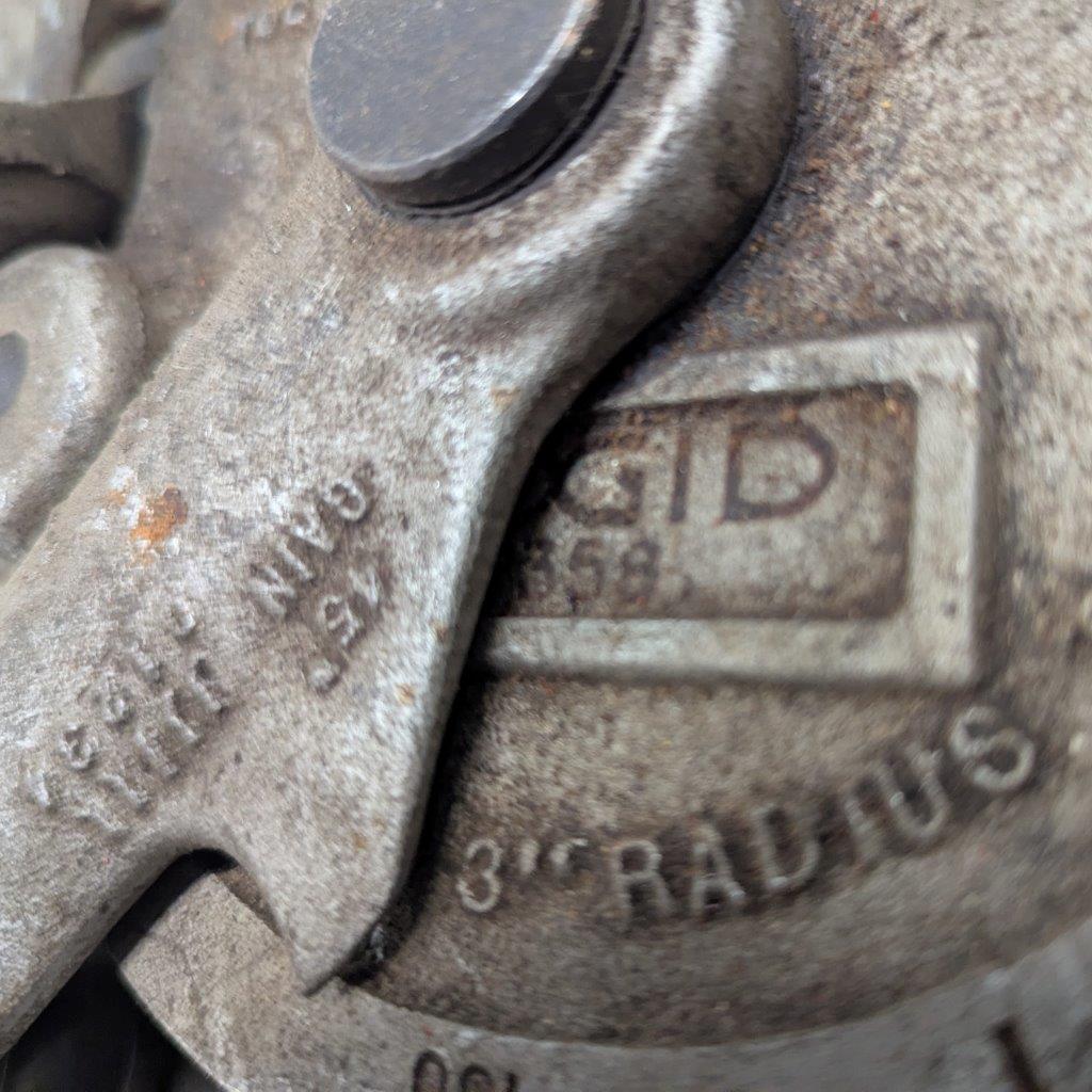 Ridgid-358-Model-Geared-Ratchet-Tube-Bender_10 | Chicago HVAC tools and supplies Close-up of a weathered metal latch with stamped numbers and a small rectangular label reading 'ID' on a dusty mechanical part.