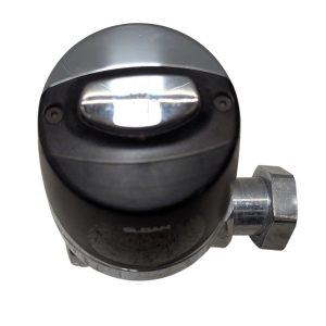 Close-up of a black circular valve housing with a chrome oval insert and a metal hose connector on the side.